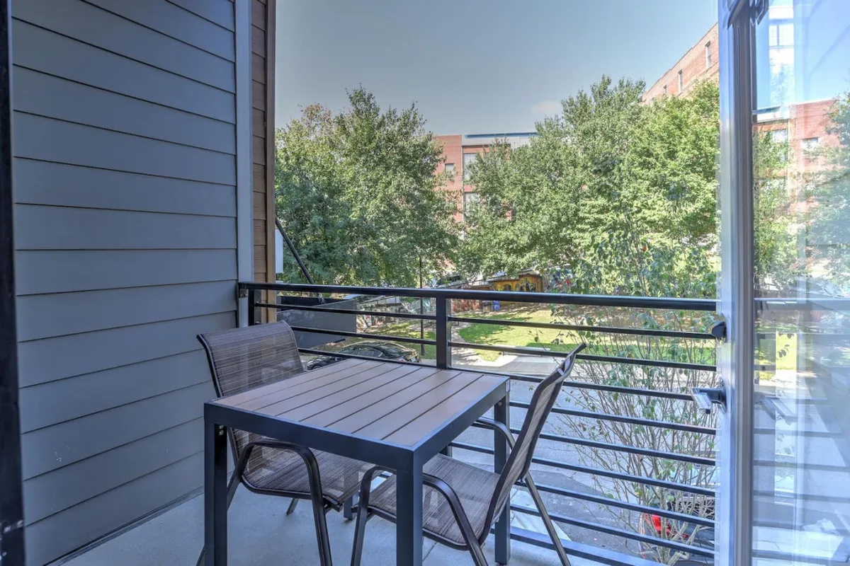 This image captures the private balcony's outdoor seating area, featuring a table and chairs with views over nearby green spaces and the city. The setting is bathed in morning sunlight, evoking a relaxed atmosphere ideal for enjoying coffee, reading, or watching the city below.