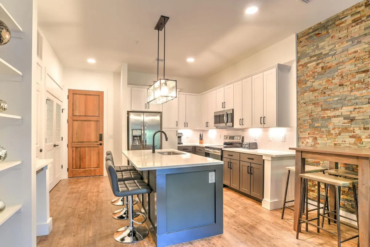 A modern kitchen island with stools is featured alongside stylish appliances and the distinctive stone accent wall. The setup encourages both casual dining and more formal entertaining, emphasizing the versatility of the open-concept layout.